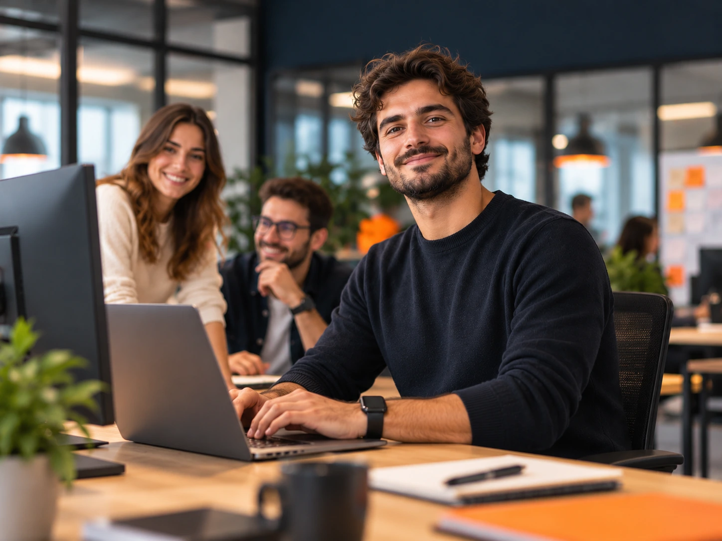 Smiling developer working on a laptop in a modern office, with teammates in the background
